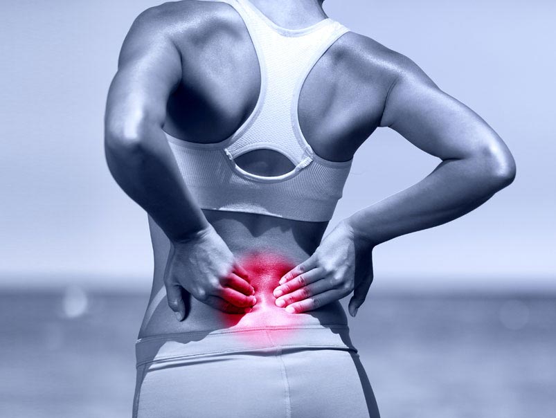 A woman wearing jogging clothes and touching her lower back with both hands and the area around her lower back is highlighted with a red circle showing that the woman has discomfort in that area and she will need the care of a professional chiropractor to help her take care of her lower back discomfort and provide her with holistic strategies for lower back health.