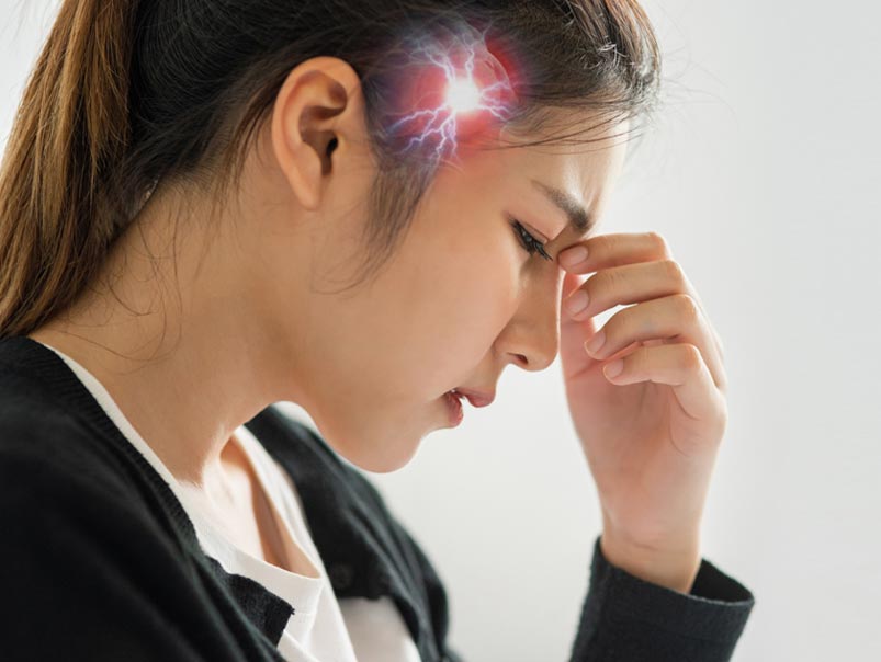 A Malaysian woman holding the top of her nose with both fingers which means that she is has a migraine and needs a professional chiropractor to provide her with innovative solutions for spinal health which can help her with migraines.